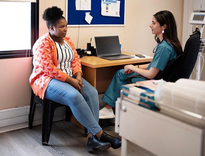 a female clinician sits in an exam room talking with an overweight female patient