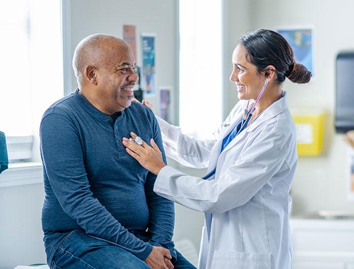 A female doctor listens to an older male patient's heart