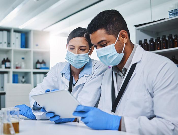 Stock. Researchers in white coats and masks review results on a tablet