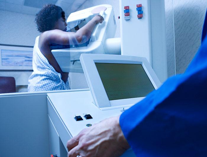 A woman stands at a machine in process of a mammogram 