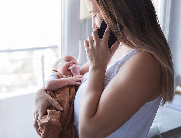A mother and holds newborn while talking on the phone