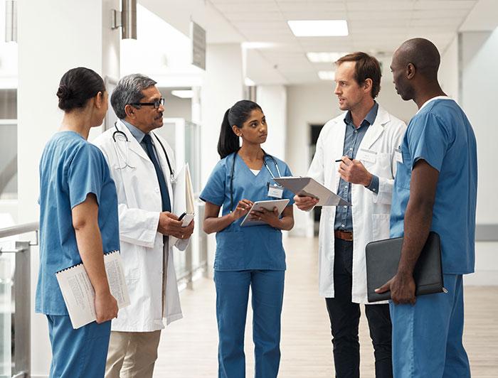 Stock. A diverse team of clinicians stands talking in a hospital hallway