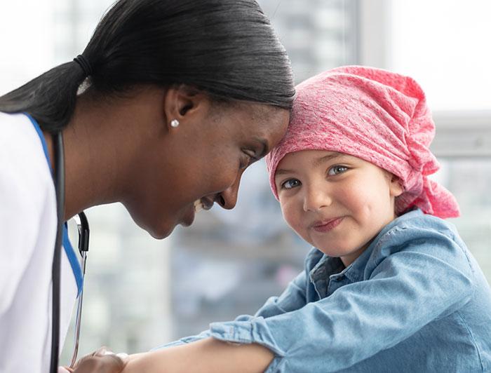 A female doctor leans forehead against forehead of young girl wearing a scarf on her head