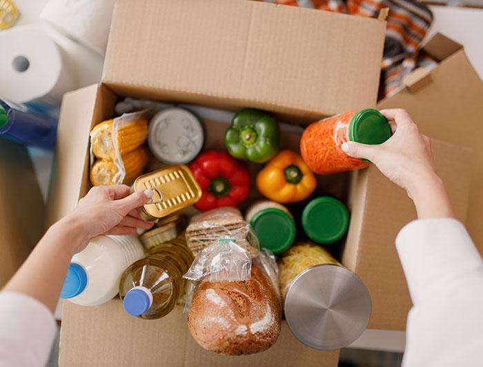 hands reach into a cardboard box filled with groceries