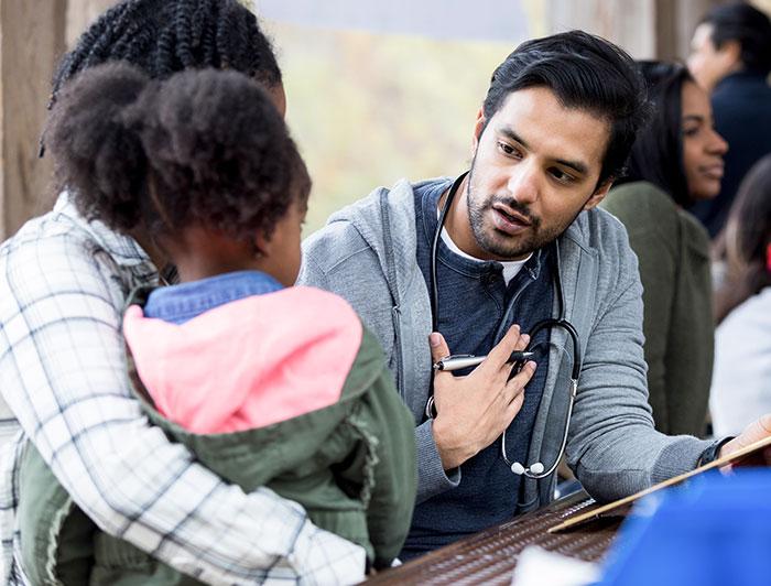 A young male physician talks to a young girl seated on her mother's lap