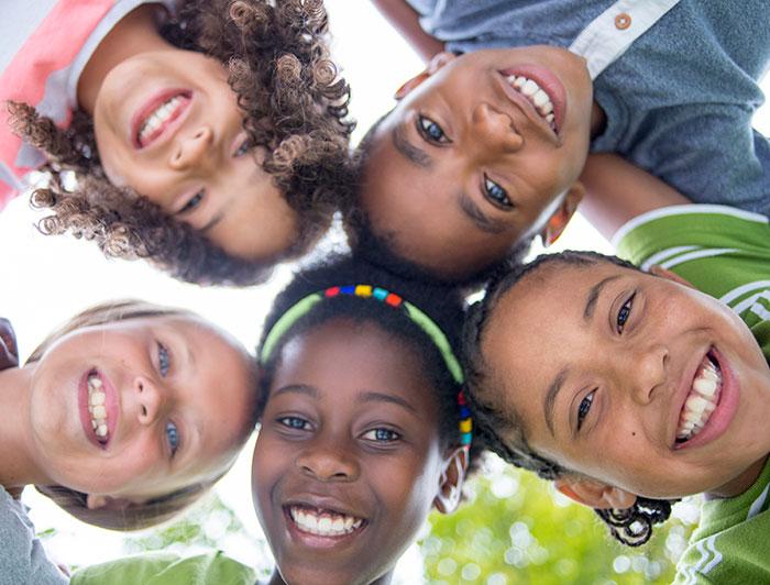 Children huddling in a circle smile down at camera in photo shot from below