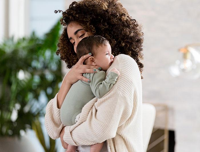 Stock image of a young curly-haired mother holding an infant against her shoulder