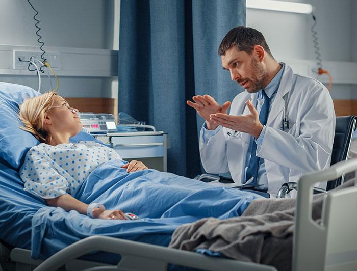 Stock image of a physician sitting at a woman's hospital bedside talking