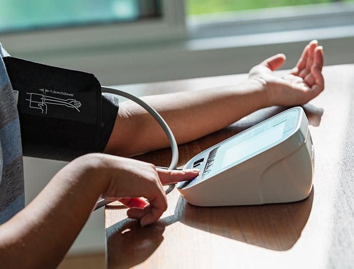 An person's arm, wrapped in a blood pressure cuff, is outstretched on a table