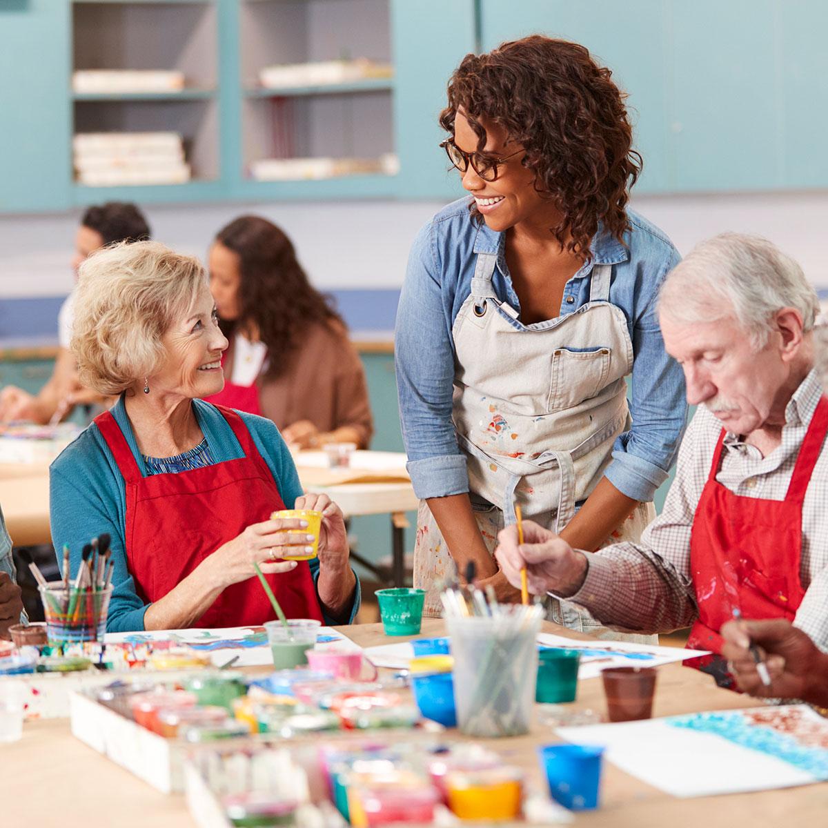 A female art teacher stands talking to an older woman seated at a craft table
