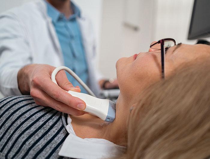 A health worker passes an ultrasound wand over a female patient's neck
