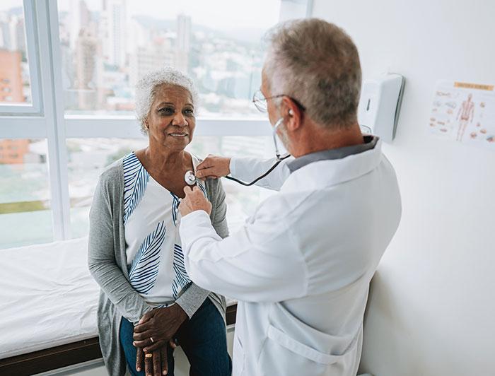 A male physician uses a stethoscope to listen to a female patient's heart 