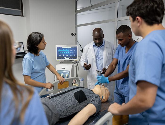 young people and a physician stand gathered around a training mannequin in a hospital bed