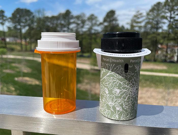A paper pill bottle is shown next to a standard plastic prescription pill bottle.