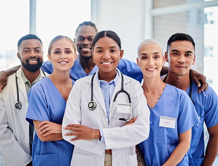 A diverse medical team of six men and women in white jackets and scrubs