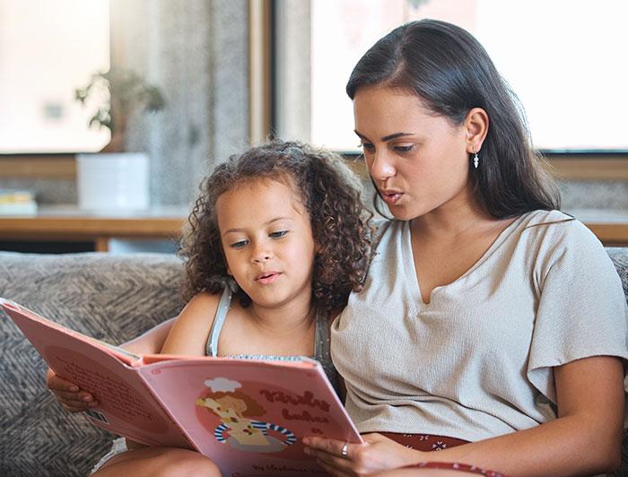 A woman and s young girl sit together on a sofa reading a children's book