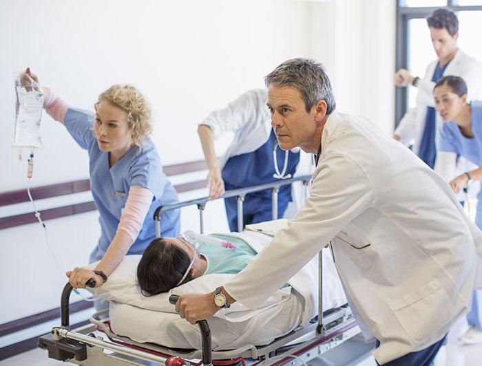 A medical team rushes a patient on a stretcher down a hospital hallway