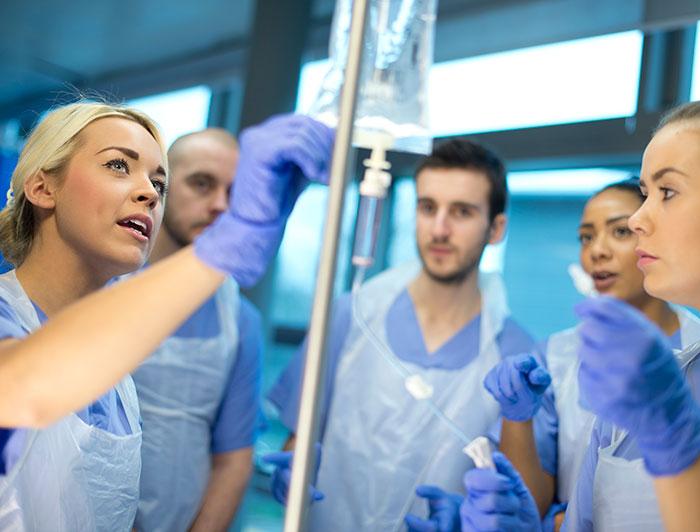 Students stand around a saline bag watching an IV demonstration