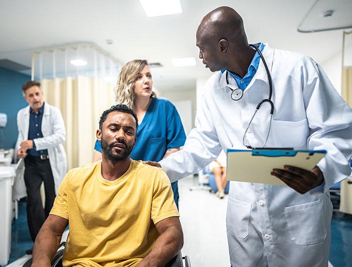 A patient being attended by three health workers sits in an emergency room 