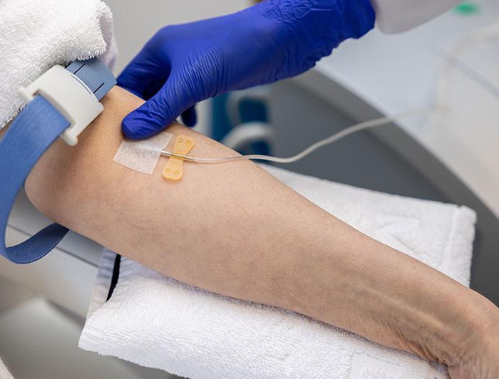 Close shot of gloved hands placing an IV line into an extended arm