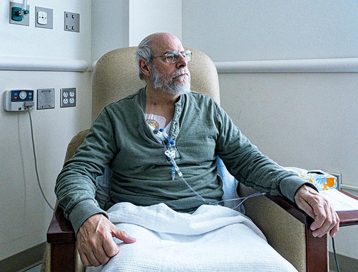 An older man sits in a hospital chair receiving an infusion