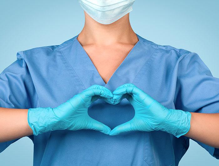 Stock image of a health worker in scrubs making a heart gesture over her chest with her hands
