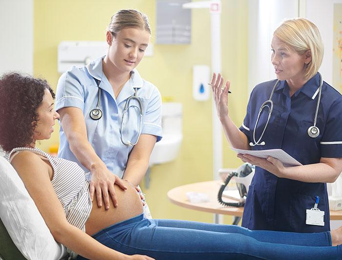 A pregnant woman on a clinic table talks with a nurse as a second nurse performs an abdominal examination