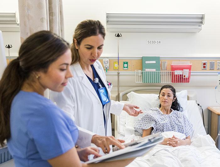 Penn Medicine Chester County Hospital. A physician and a nurse review a patient's chart while the patient sits in bed.