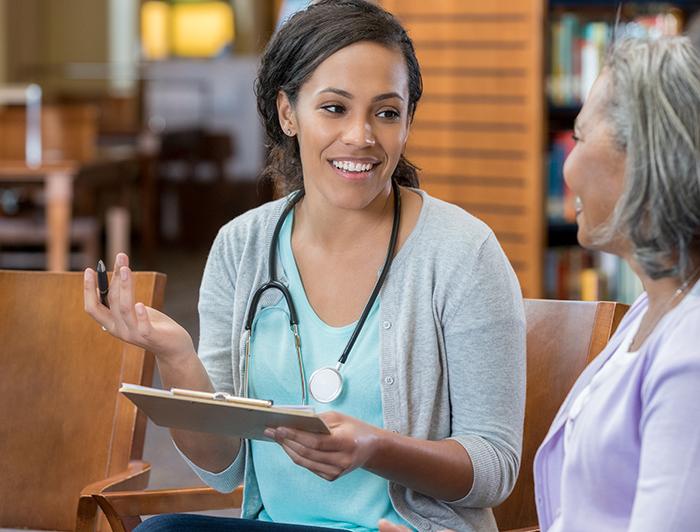 A female clinician wearing a stethoscope talks to an older female patient